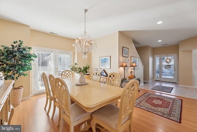 dining area featuring light wood-type flooring, french doors, and a notable chandelier