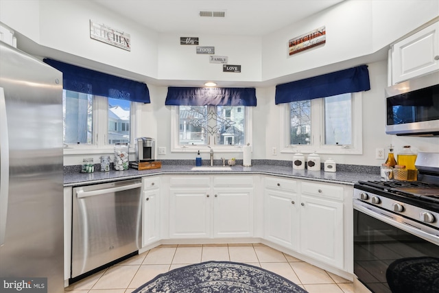 kitchen featuring stainless steel appliances, a towering ceiling, white cabinetry, light tile patterned flooring, and sink