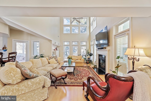 living room with ceiling fan, hardwood / wood-style floors, a towering ceiling, and a high end fireplace