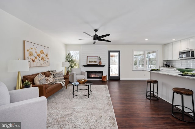 living room featuring a fireplace, ceiling fan, plenty of natural light, and dark wood-type flooring