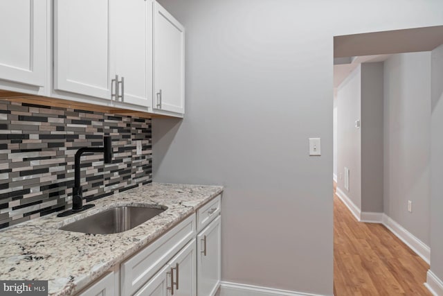 kitchen featuring white cabinetry, sink, light stone counters, decorative backsplash, and light wood-type flooring