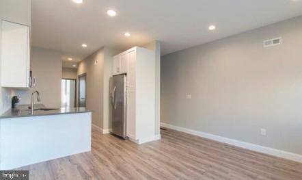 kitchen with white cabinets, light wood-type flooring, sink, and stainless steel refrigerator