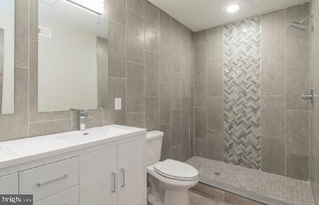 bathroom featuring a tile shower, vanity, toilet, and tile walls