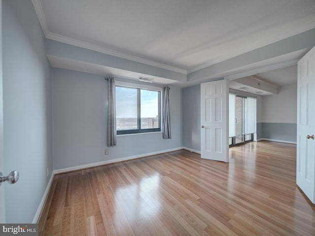 empty room featuring ornamental molding, light wood-type flooring, visible vents, and baseboards