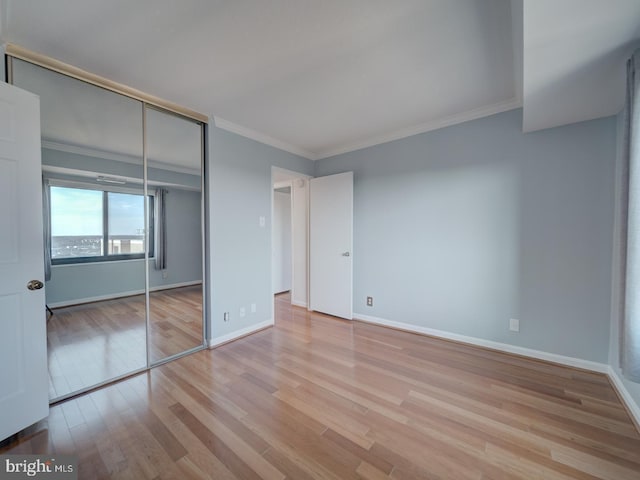 unfurnished bedroom featuring ornamental molding, a closet, light wood-style flooring, and baseboards