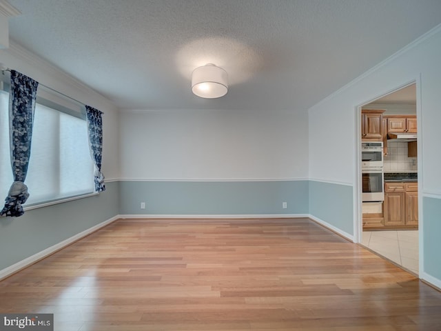 empty room featuring light wood-style floors, ornamental molding, a textured ceiling, and baseboards