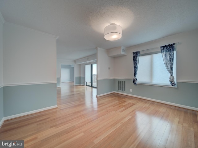 spare room featuring light wood finished floors, visible vents, baseboards, crown molding, and a textured ceiling