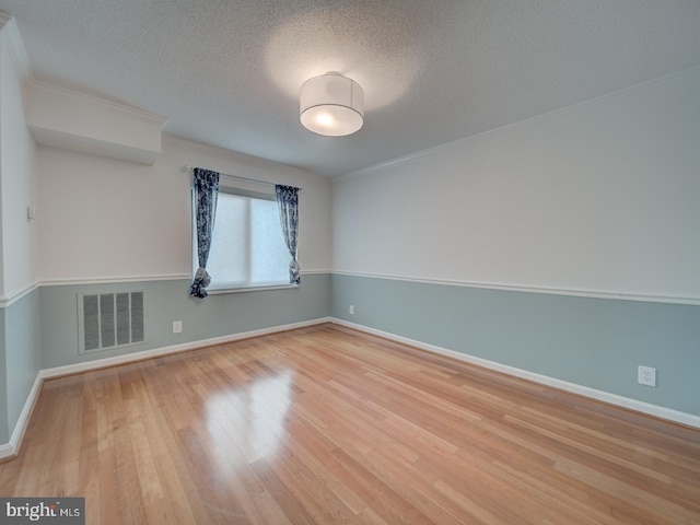 empty room featuring visible vents, a textured ceiling, and wood finished floors