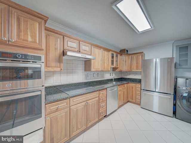 kitchen featuring under cabinet range hood, washer / dryer, appliances with stainless steel finishes, decorative backsplash, and glass insert cabinets