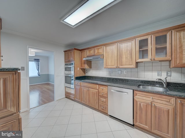 kitchen with stainless steel appliances, glass insert cabinets, a sink, dark stone counters, and under cabinet range hood