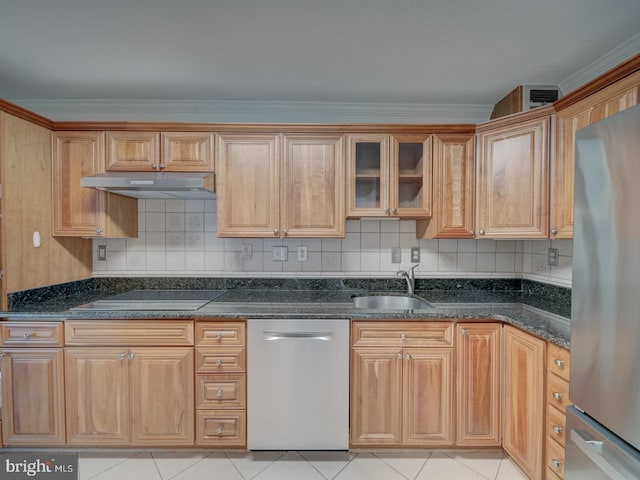 kitchen featuring dark stone counters, glass insert cabinets, stainless steel appliances, under cabinet range hood, and a sink