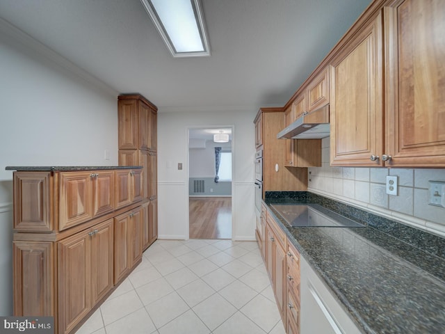 kitchen featuring decorative backsplash, brown cabinetry, light tile patterned flooring, dark stone counters, and black electric cooktop