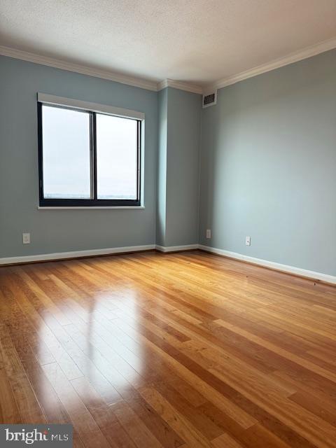 empty room with baseboards, crown molding, visible vents, and light wood-style floors