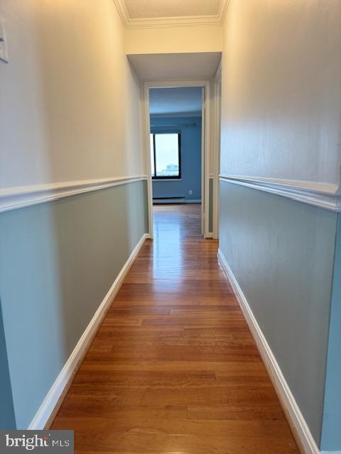 corridor featuring a baseboard heating unit, baseboards, ornamental molding, and wood finished floors