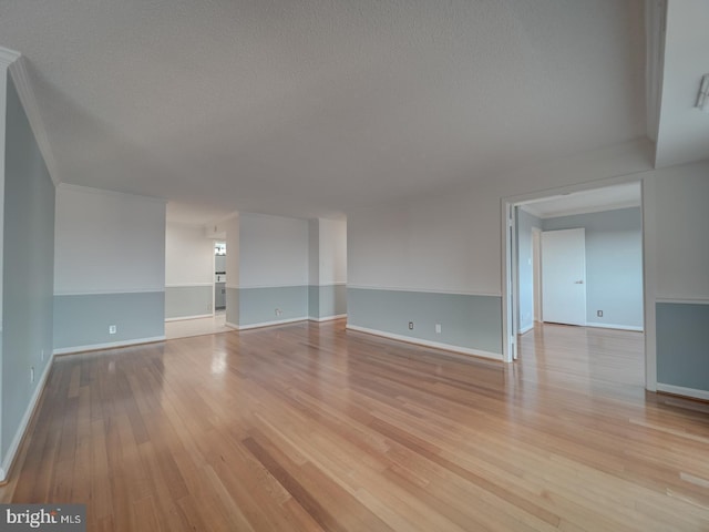 spare room featuring a textured ceiling, crown molding, light wood-type flooring, and baseboards