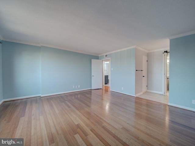 unfurnished room featuring baseboards, a barn door, ornamental molding, and light wood-style floors