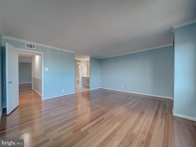 interior space with a barn door, baseboards, visible vents, ornamental molding, and light wood-type flooring