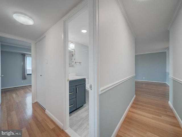 hallway with ornamental molding, light wood-type flooring, and baseboards