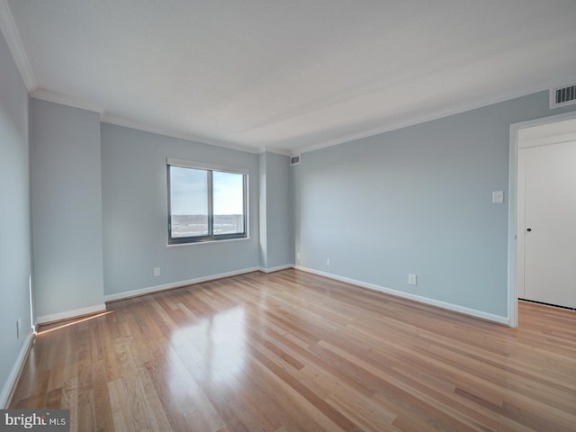 empty room with light wood-style floors, visible vents, baseboards, and ornamental molding