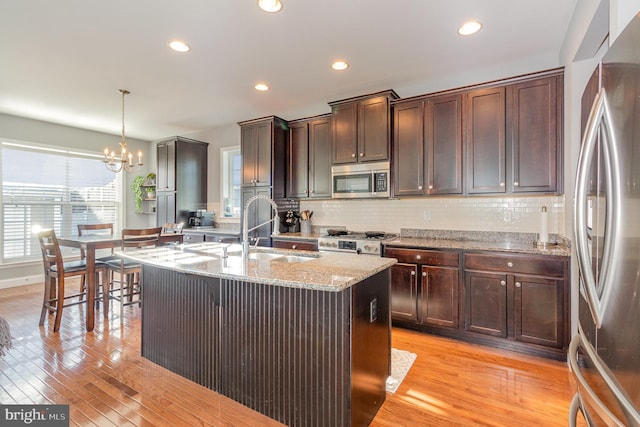 kitchen with sink, a chandelier, pendant lighting, a center island with sink, and appliances with stainless steel finishes