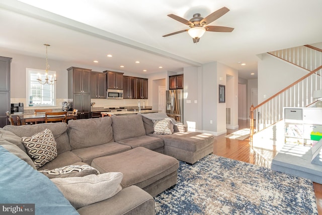 living room with ceiling fan with notable chandelier and light hardwood / wood-style flooring