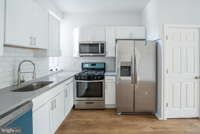 kitchen featuring sink, backsplash, appliances with stainless steel finishes, white cabinets, and light wood-type flooring