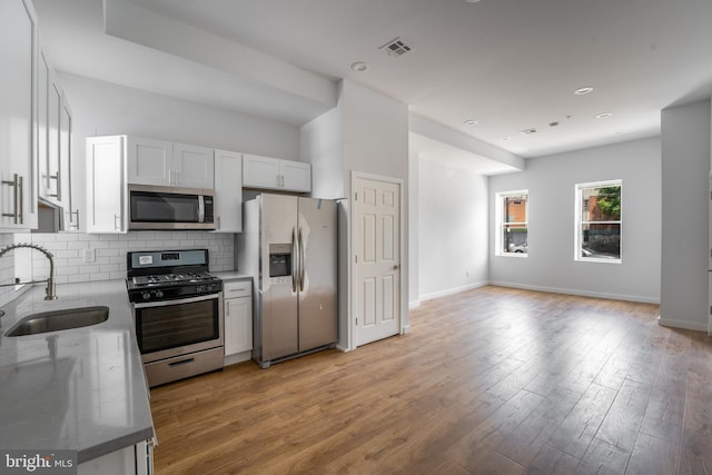 kitchen featuring sink, backsplash, light hardwood / wood-style floors, white cabinets, and appliances with stainless steel finishes