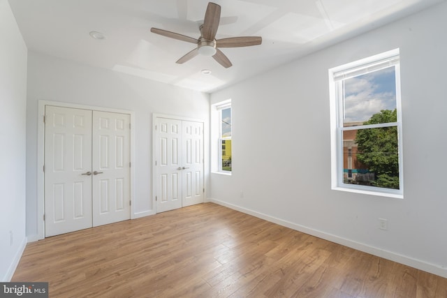 unfurnished bedroom featuring multiple windows, ceiling fan, light hardwood / wood-style floors, and two closets