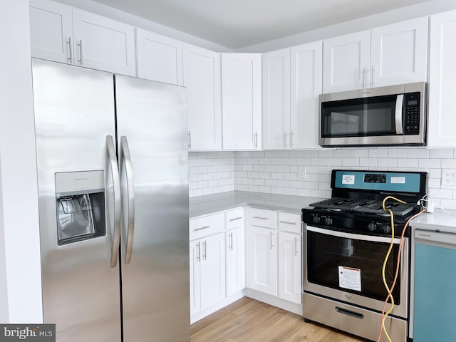 kitchen with decorative backsplash, stainless steel appliances, white cabinetry, and light hardwood / wood-style floors