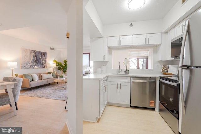 kitchen with a sink, white cabinetry, stainless steel appliances, light wood-style floors, and light countertops