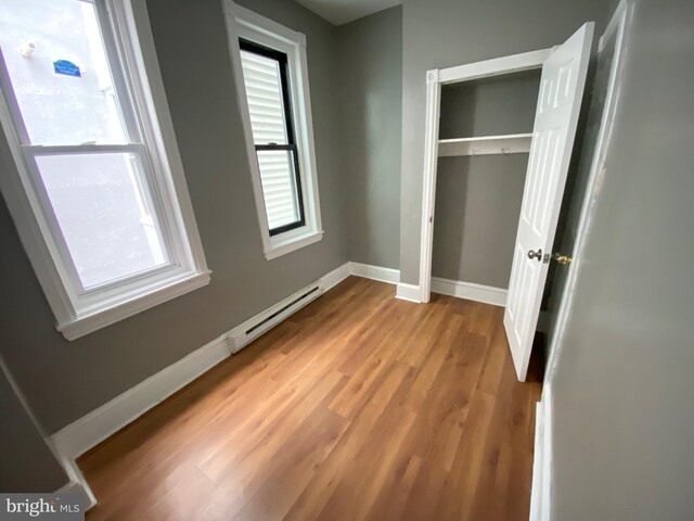 unfurnished bedroom featuring a baseboard radiator, a closet, and light hardwood / wood-style floors