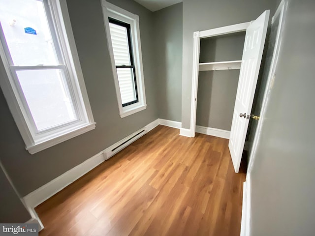 unfurnished bedroom featuring baseboard heating, a closet, and light wood-type flooring