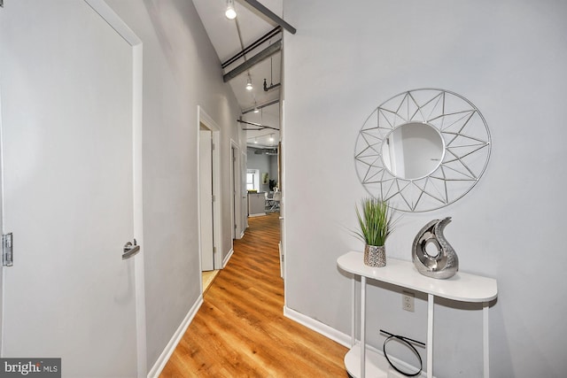 hall featuring rail lighting, a towering ceiling, baseboards, and wood finished floors