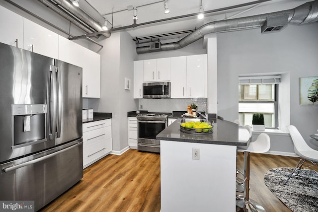 kitchen featuring appliances with stainless steel finishes, a kitchen breakfast bar, hardwood / wood-style floors, white cabinets, and a high ceiling