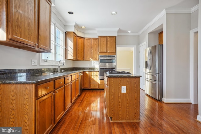 kitchen with a center island, dark stone countertops, hardwood / wood-style floors, appliances with stainless steel finishes, and ornamental molding