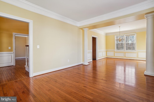 unfurnished room featuring hardwood / wood-style floors, decorative columns, ornamental molding, and an inviting chandelier