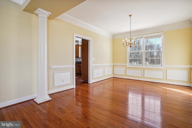 unfurnished dining area with decorative columns, ornamental molding, wood-type flooring, and a notable chandelier