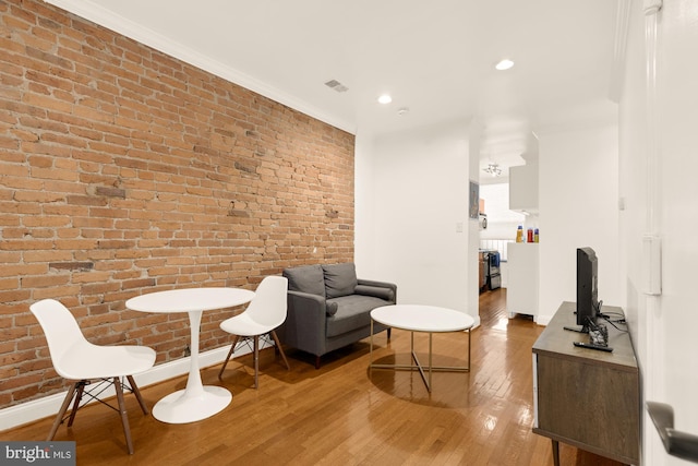 living area featuring hardwood / wood-style floors, ornamental molding, and brick wall