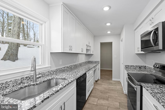 kitchen with appliances with stainless steel finishes, sink, white cabinetry, light stone countertops, and built in desk