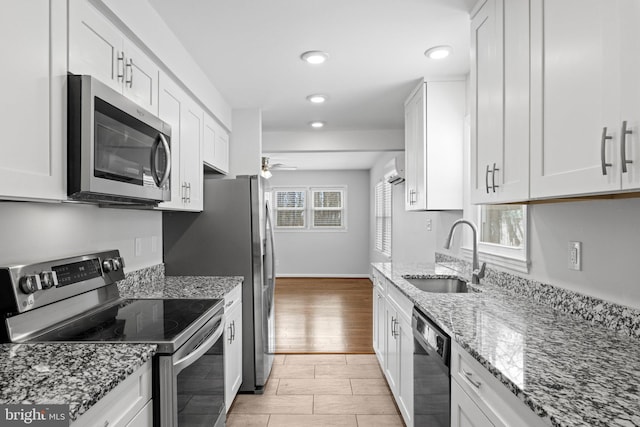 kitchen featuring light stone countertops, appliances with stainless steel finishes, white cabinetry, sink, and ceiling fan