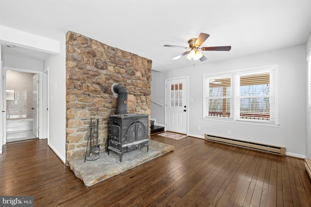 unfurnished living room with ceiling fan, baseboard heating, dark wood-type flooring, and a wood stove