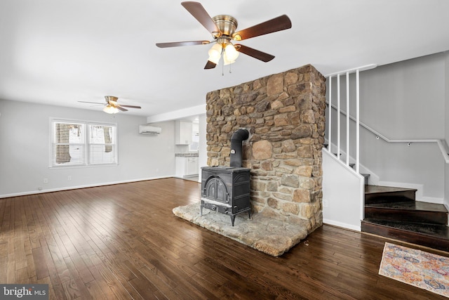 unfurnished living room with ceiling fan, a wood stove, dark hardwood / wood-style floors, and a wall mounted air conditioner