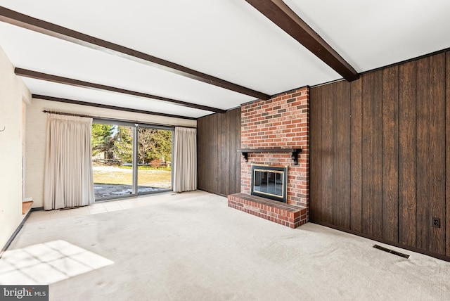 unfurnished living room featuring beam ceiling, light colored carpet, a brick fireplace, and wood walls