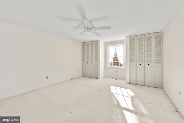 unfurnished bedroom with light carpet, two closets, ceiling fan, and crown molding