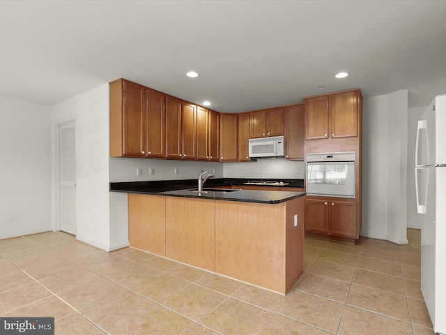 kitchen with white appliances, light tile patterned floors, a peninsula, a sink, and dark countertops