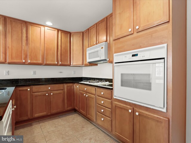 kitchen featuring white appliances, dark stone countertops, light tile patterned floors, recessed lighting, and brown cabinets