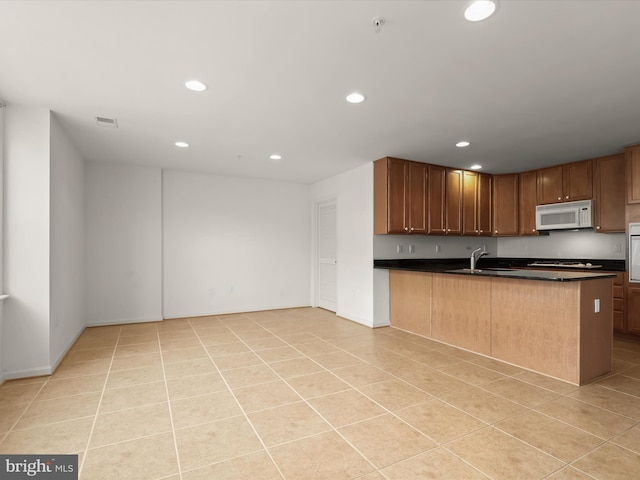 kitchen with white microwave, dark countertops, recessed lighting, light tile patterned flooring, and a sink