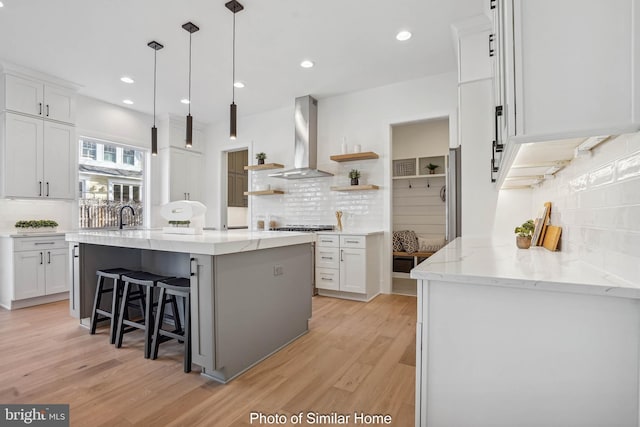 kitchen with white cabinets, backsplash, a kitchen island, and wall chimney range hood