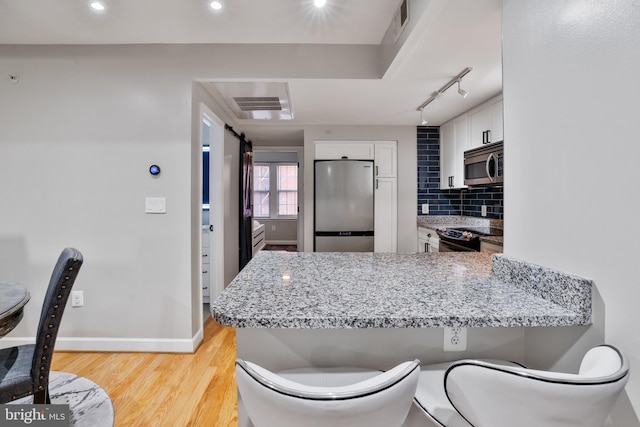 kitchen with stainless steel appliances, light stone counters, light hardwood / wood-style flooring, backsplash, and white cabinets