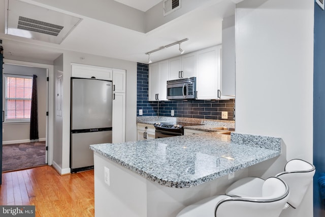 kitchen featuring a kitchen breakfast bar, kitchen peninsula, white cabinets, and stainless steel appliances